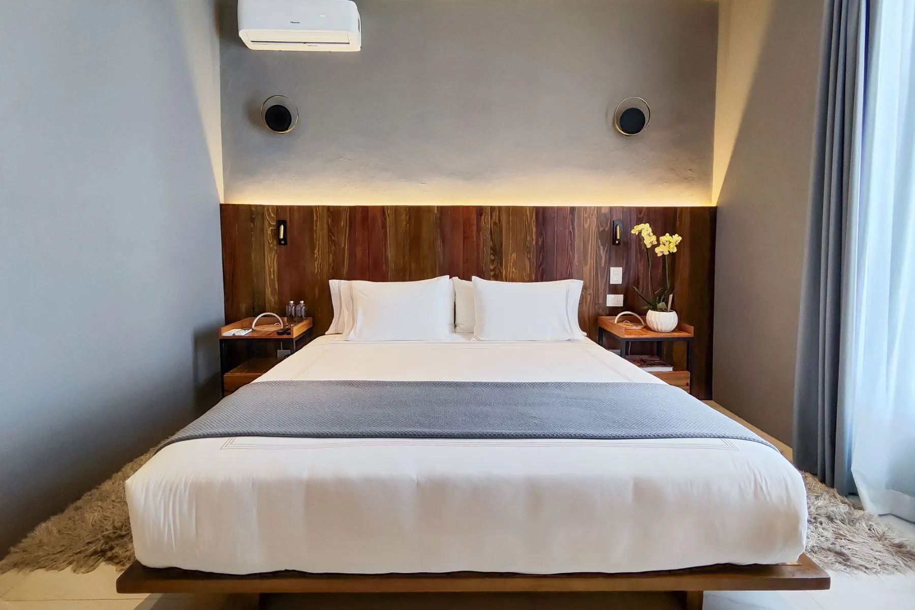 Bedroom with a king bed, dark wood headboard, warm cove lighting and bedside trays