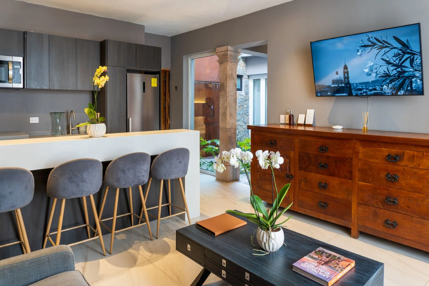 Modern grey kitchen with a white bar counter and stools opening to a lounge beside a cantera stone column